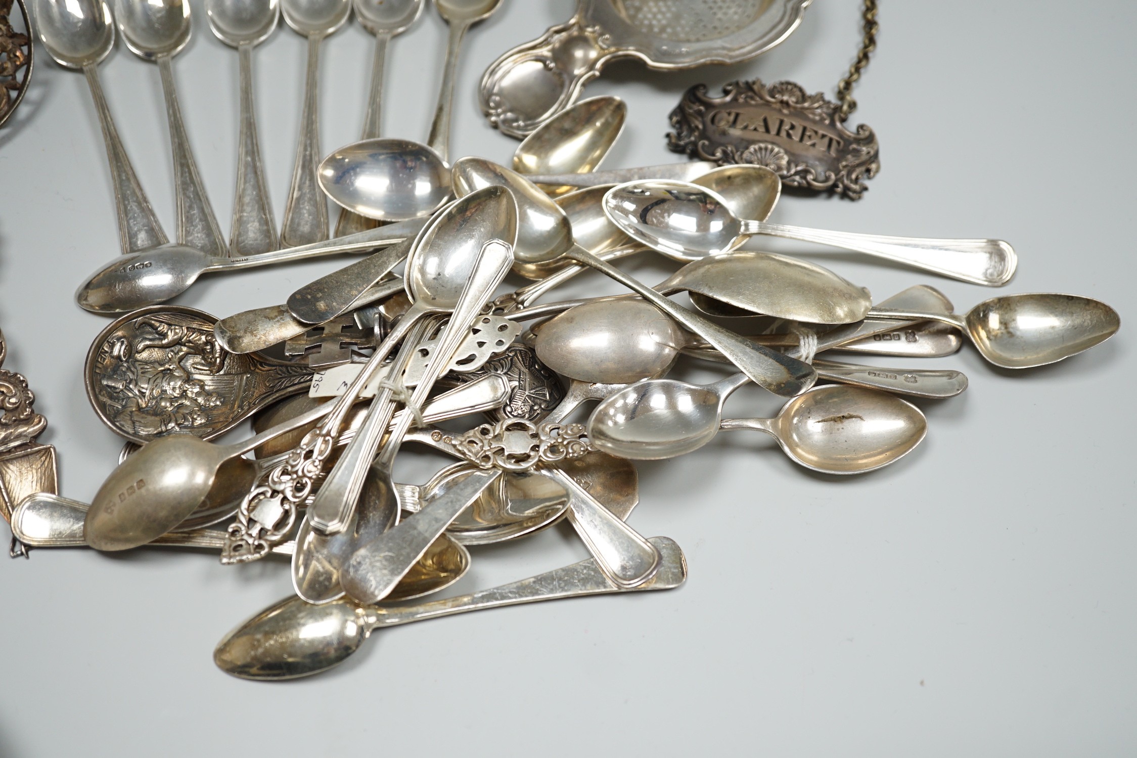 A group of mixed silver and white metal items including flatware, Dutch fish slice, German 800 tea strainer, George IV 'Claret' wine label, etc. and a plated spoon.